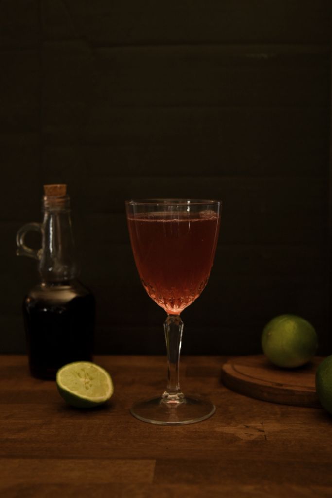 finished blueberry lime cocktail with limes and a bottle in the back-round 