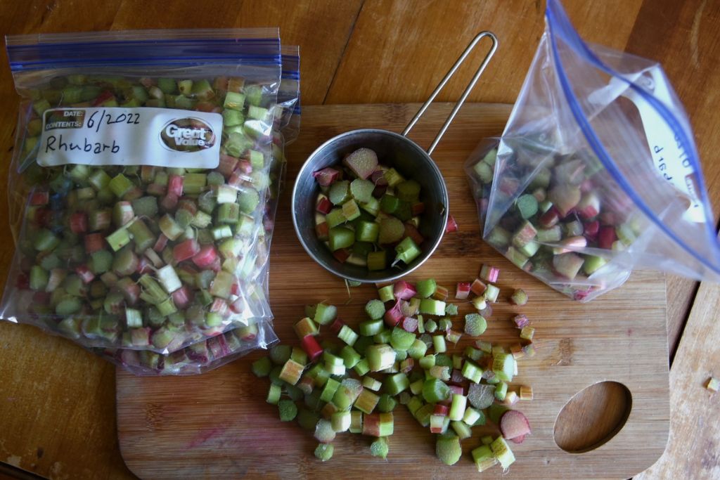 a pile of chopped rhubarb, a measuring cup, a stack of freezer bags and an open freezer bag sitting on a cutting board