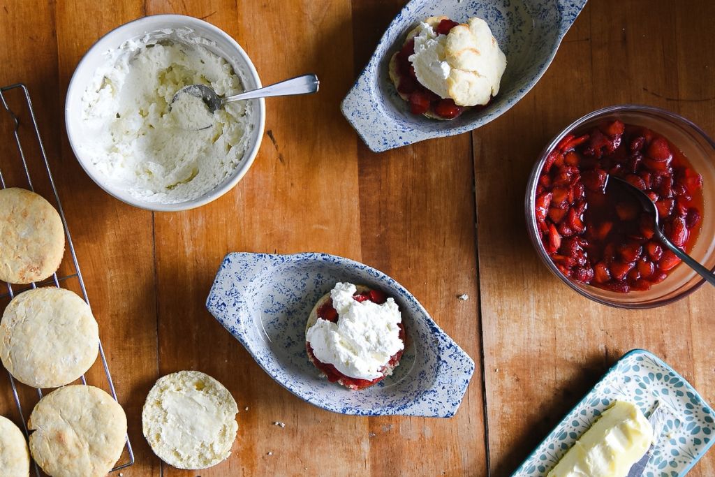 a finished strawberry shortcake with the ingredients around it and another one that has strawberries and homemade whipped cream