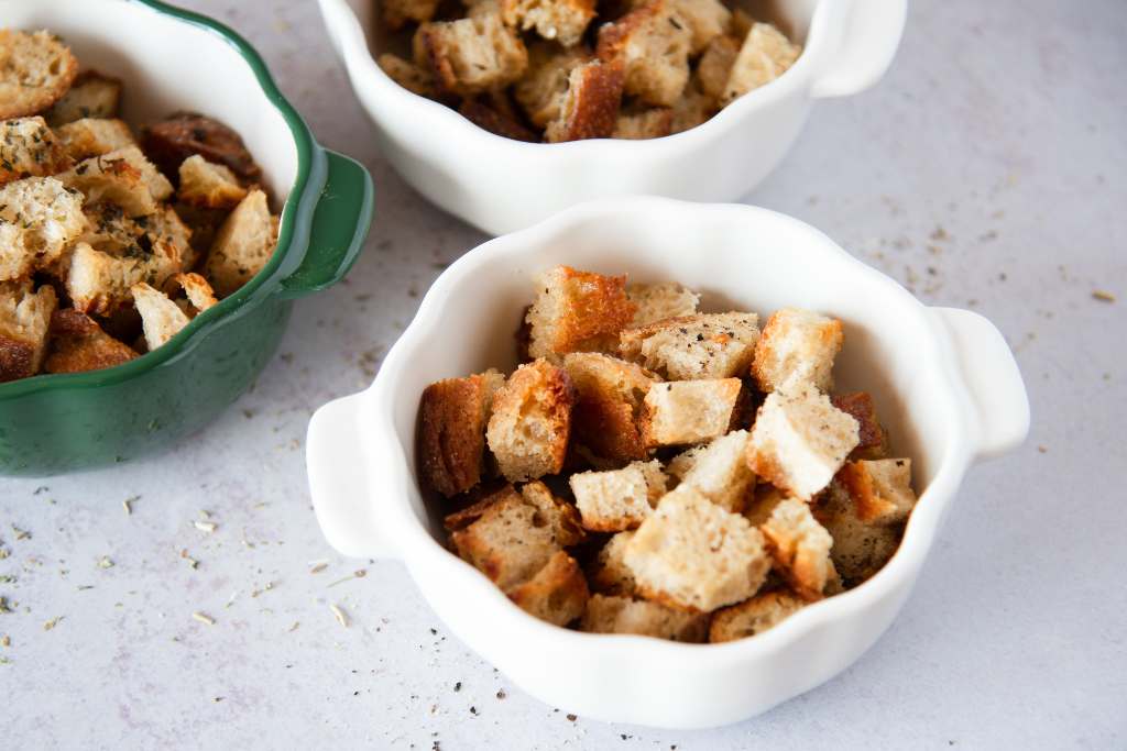 a closeup of a dish of homemade croutons, you can see part of two other dishes behind it 