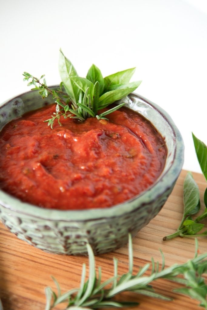 a close up of a dish of pizza sauce there are fresh herbs in the sauce and some set around the bowl
