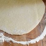 rolled out pizza dough on a table with flour