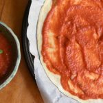 a dish of pizza sauce with a pizza crust next to it, the crust as sauce on it