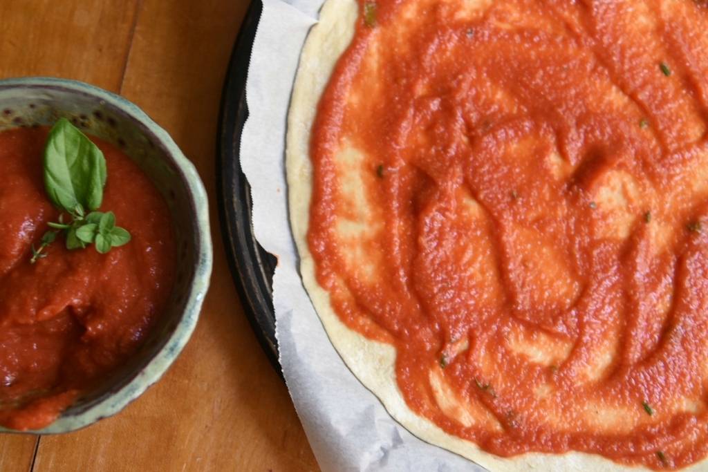 a dish of sauce sitting next to a pizza crust that also has sauce on it