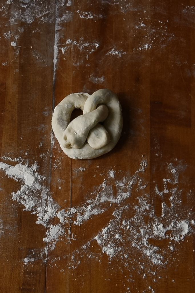 a finished uncooked pretzel sitting on the table with flour around it