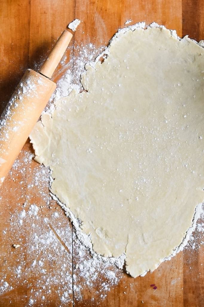 a rolled out pie crust on the table with a rolling pin next to it,and some flour.