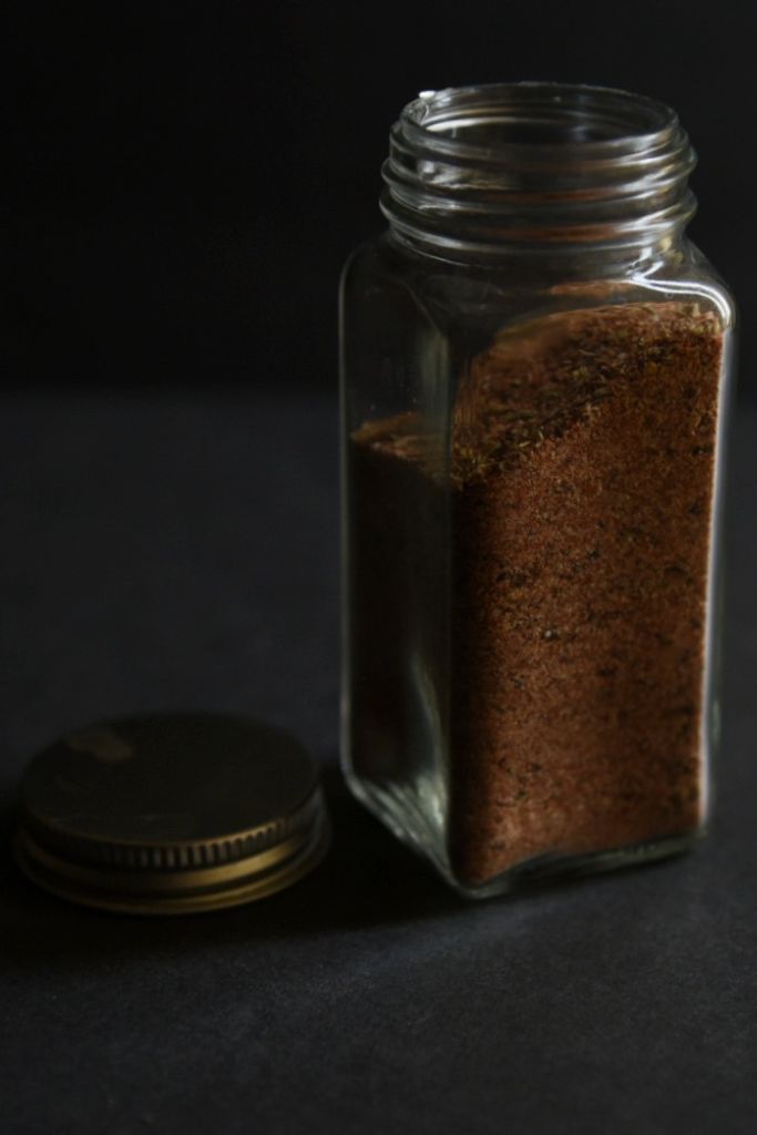 a spice bottle full of cajun seasoning with a cover sitting next to it.
