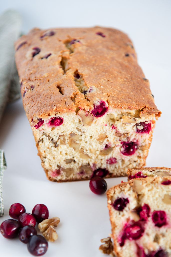 a loaf of cranberry bread that has been sliced, there are some whole cranberries and chopped nuts around it 