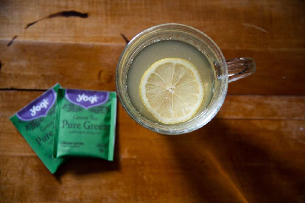 a cup of cold-fighting tea with lemon slice in it. And two bag of green tea next to it 