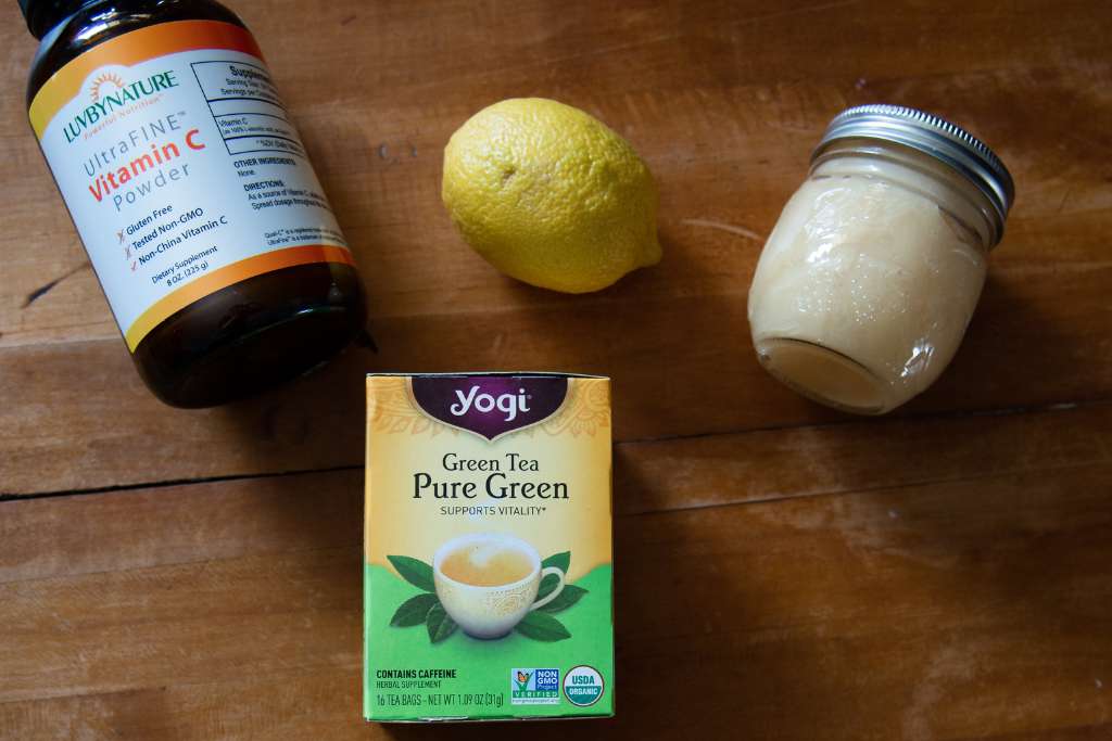 a box of tea, with a whole lemon, a jar honey and jar of vitamin C above it