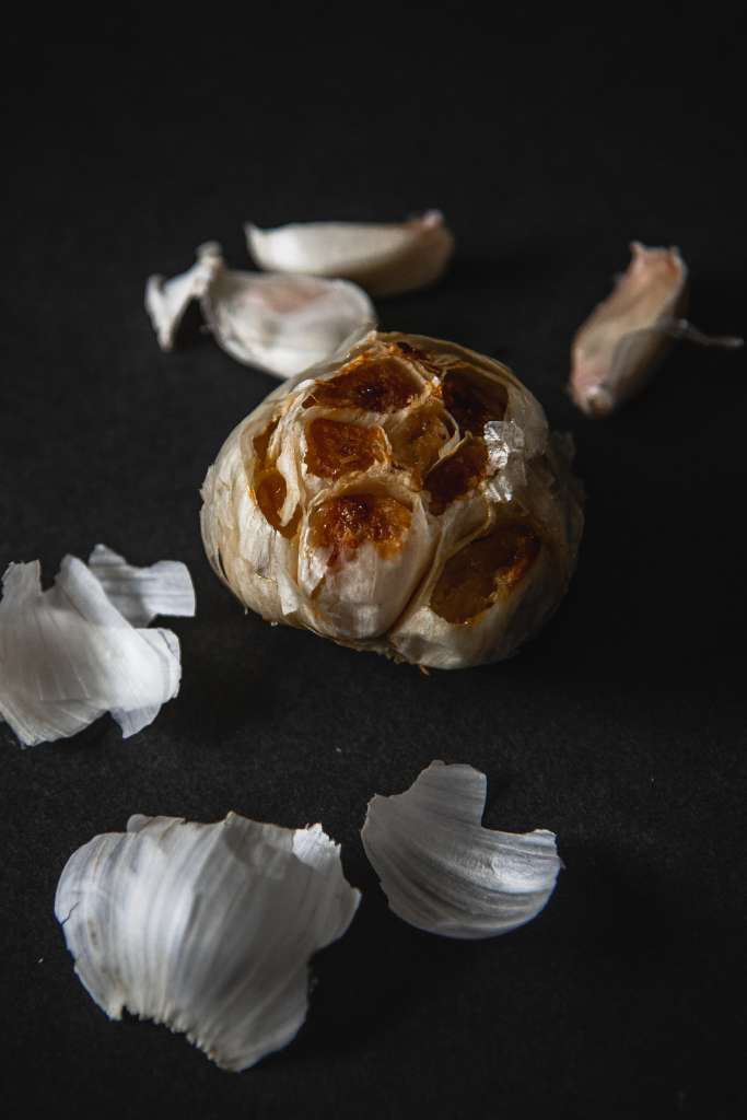 close up of a head of roast garlic with home garlic cloves behind it