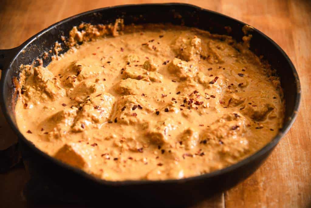 a pan of Indian Butter Chicken, with red pepper flakes sprinkled on top