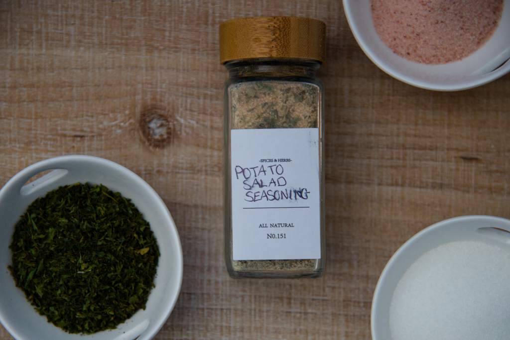 a bottle of potato salad seasoning, with three little dishes next to it, one full of salt, one full of parsley and one full of sugar