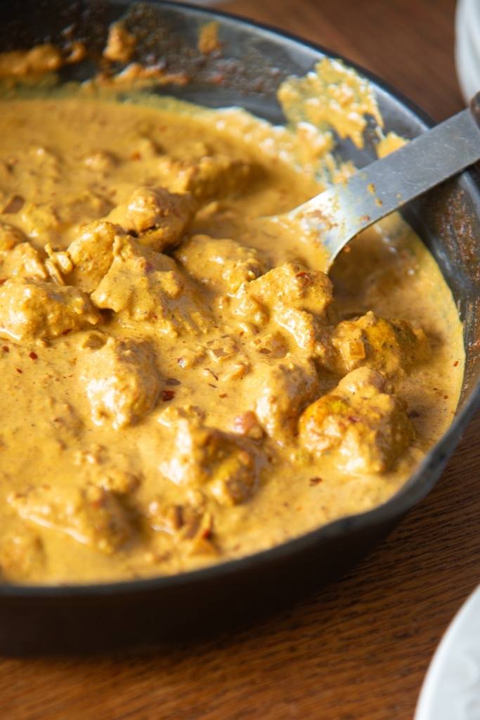 a pan of butter chicken with a spoon in it