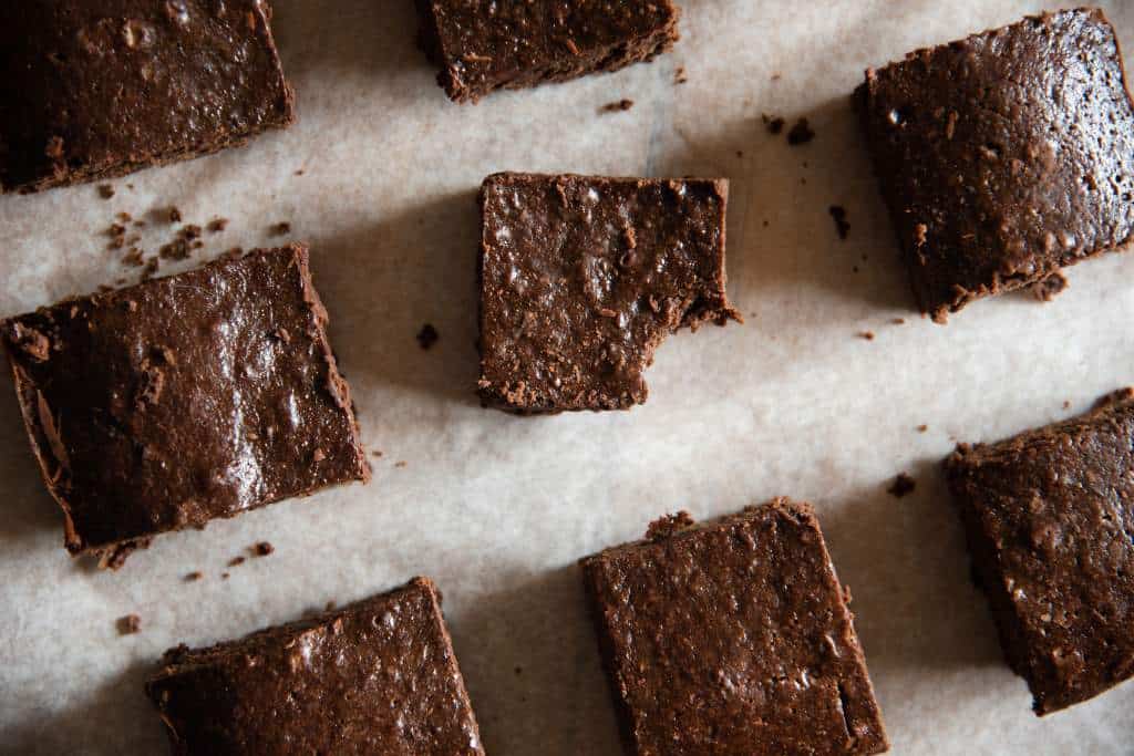 cut sourdough brownies spaced out on a piece of parchment paper, the brownie in the middle has  bit taken out of it