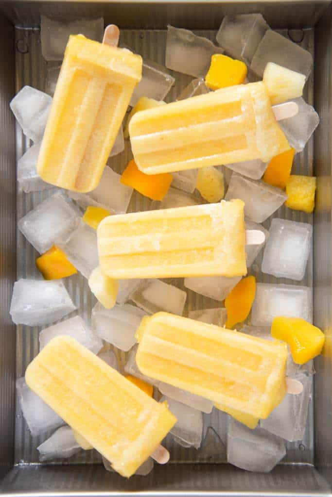 a sideways picture of five popsicles in a dish of ice and chunks of fruit