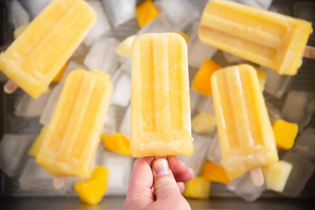 someone holding a popsicle above a dish of popsicels and ice. There are some chunks of fruit with the ice as well