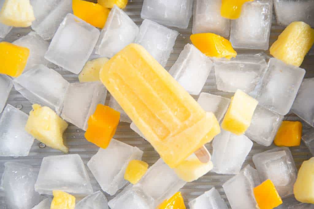 a close up of a popsicle on ice, there are some chunks of fruit around it as well