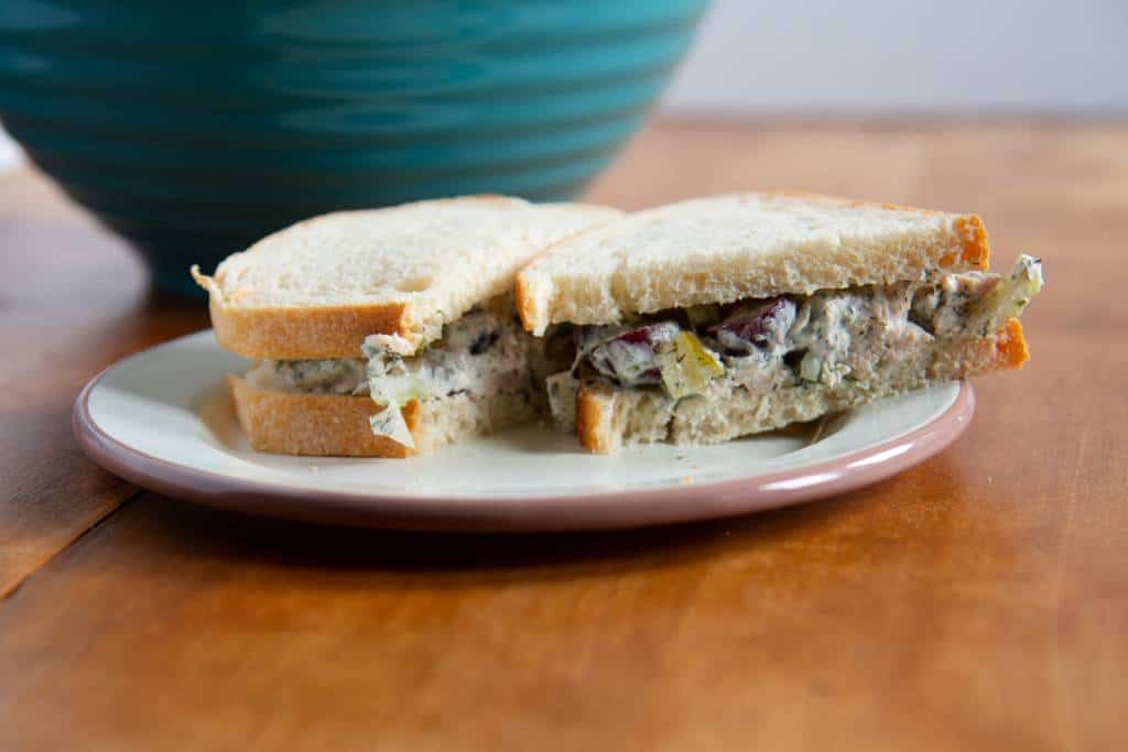 a cut sandwich on a plate, one half in turned so you can see the inside. There is a blue bowl in the background 