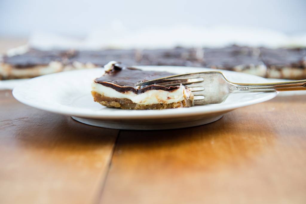 a no-bake cheesecake bar on white plate with a folk, cuting into it 