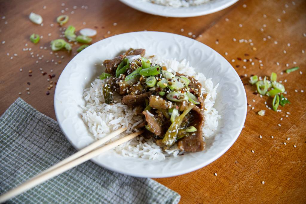 an angled shot of a bowl of mongolian rice with chopsticks stuck in it. There is a napkin in front of the bowl, and you can see a little part of another bowl behind it