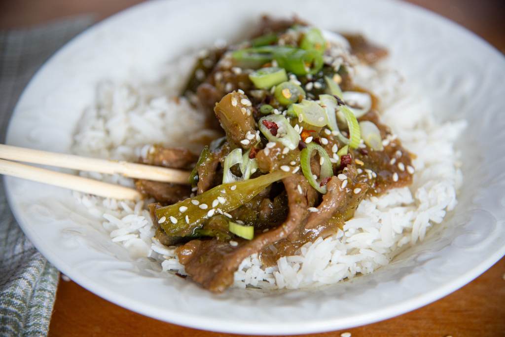 a close up of a bowl of mongolian beef and rice with a pair of chopsticks stuck in it 