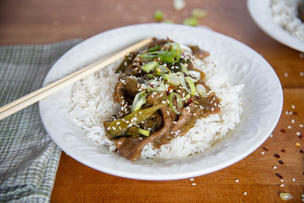 a bowl of rice and mongolian beef, there are chopsticks in the bowl and a towel/napkin next to it 