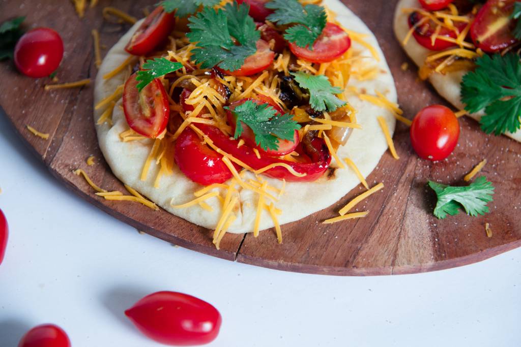 a close up of a open sandwiches, with with cheese, tomatoes and cilantro around it 