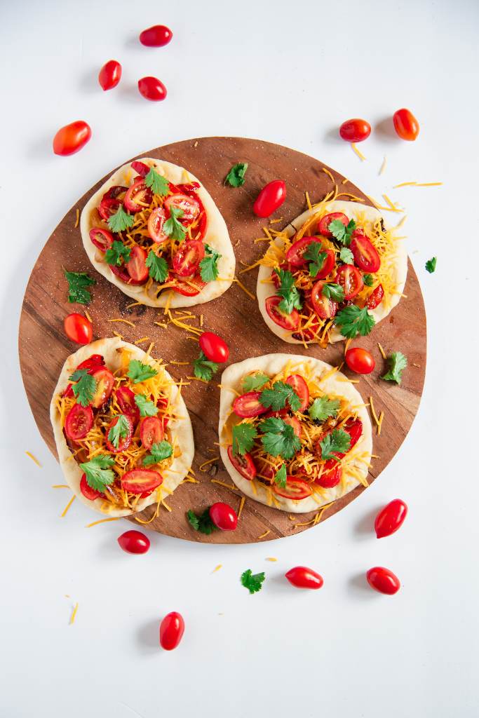 a plate with four sandwiches on it, there are some cherry tomatoes, cilantro and cheese, around them 