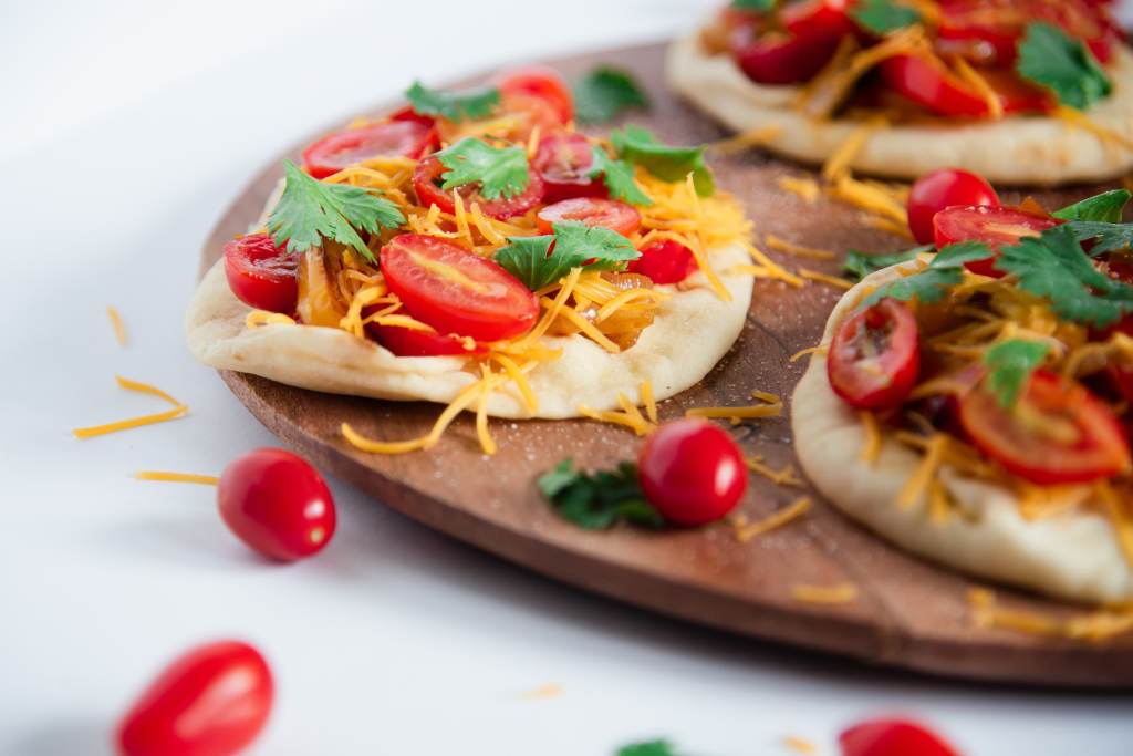 an up close picture on an open=faced sandwich, with some cheese and cherry tomatoes around, you can partially see two other sandwiches in the picture as well