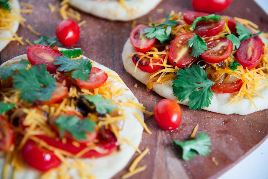 a sandwich on a wooden plate, there two other sandwiches around it, and some cherry tomatoes and cilantro by it 