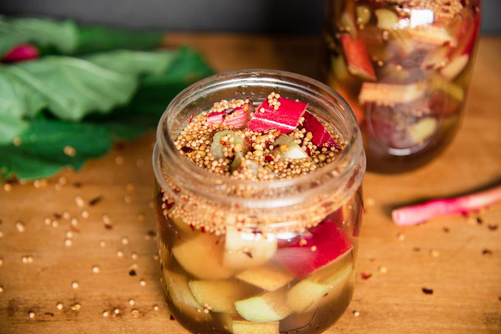 an overhead shot of a jar of pickled rhubarb, you can see another jar and some rhubarb leaves behind it 