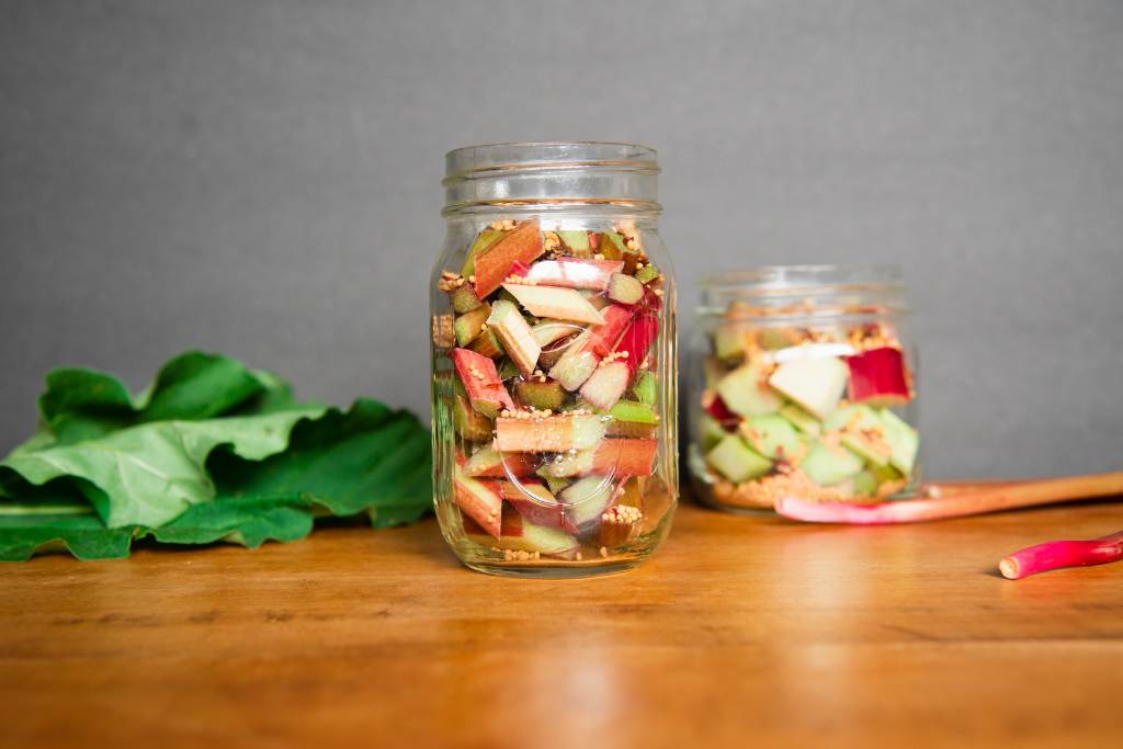 two canning jars full of rhubarb pieces, there are some rhubarb leaves and stalks next to well