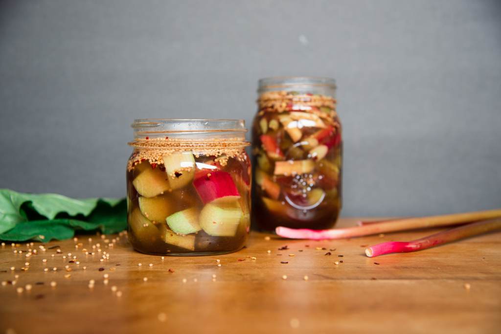 two jars of pickled rhubarb with some leaves and stalks and spices around them