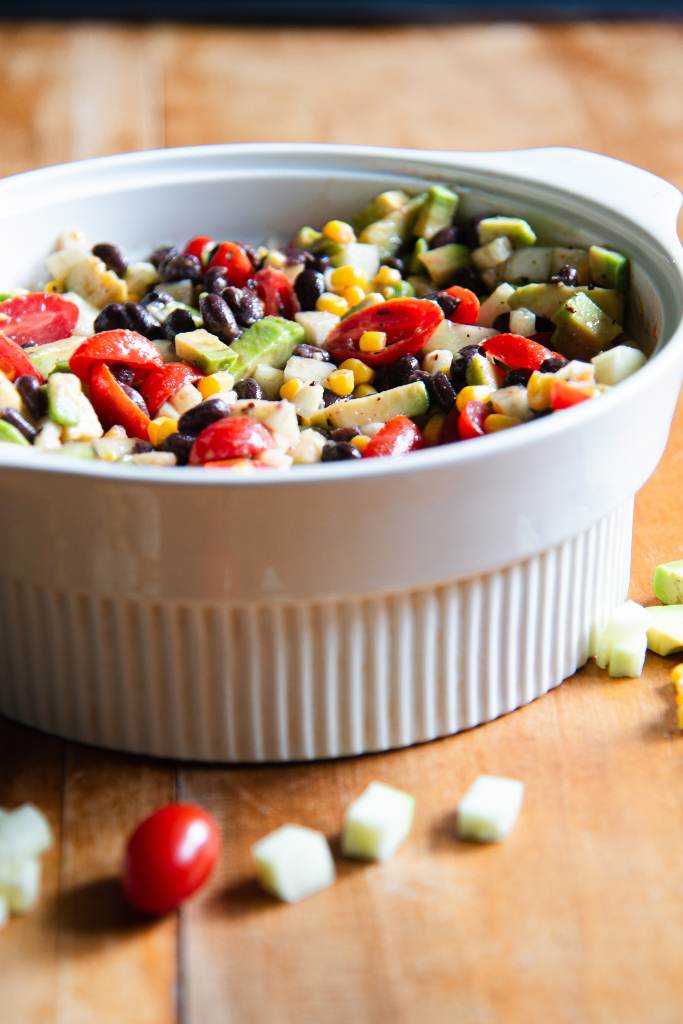 a side shot of a white bowl of avocado salad, you can see a very tiny bit of some avocado and corn next to the bowl