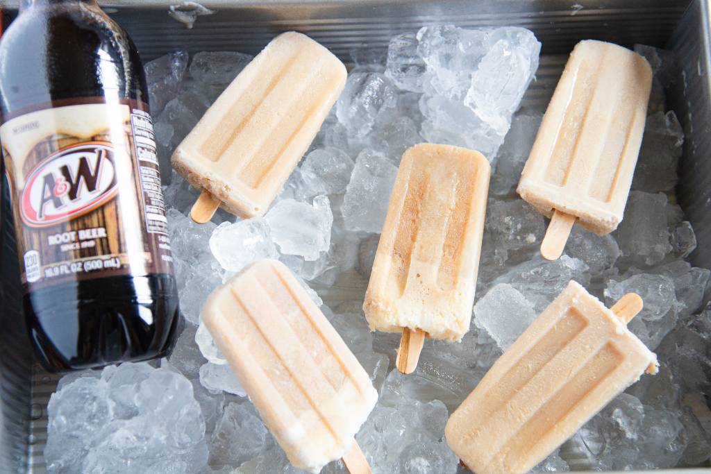 five ice cream bars in a metal dish of ice with a bottle of A&W root beer in the dish as well on the left side