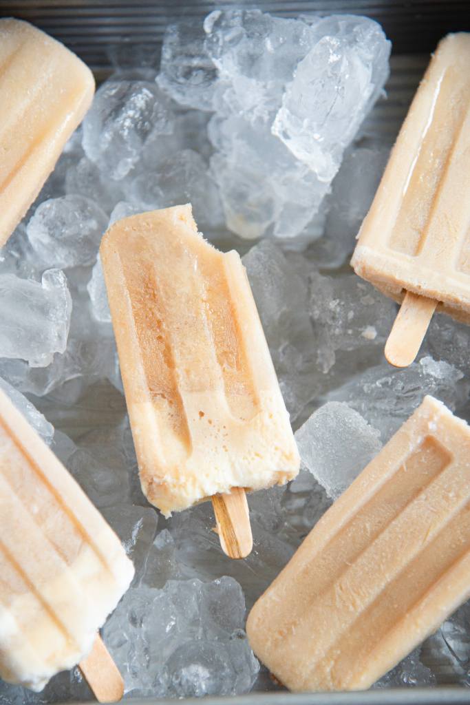 five root beer float ice cream bars in a pan of ice, the middle bar has a bite taken out of it