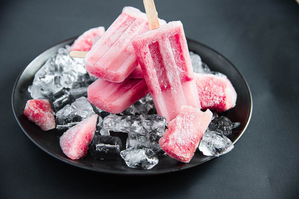 three popsicles stack on top each other with another popsicels linded again them, on a plate with ice and frozen watermelon chunks 