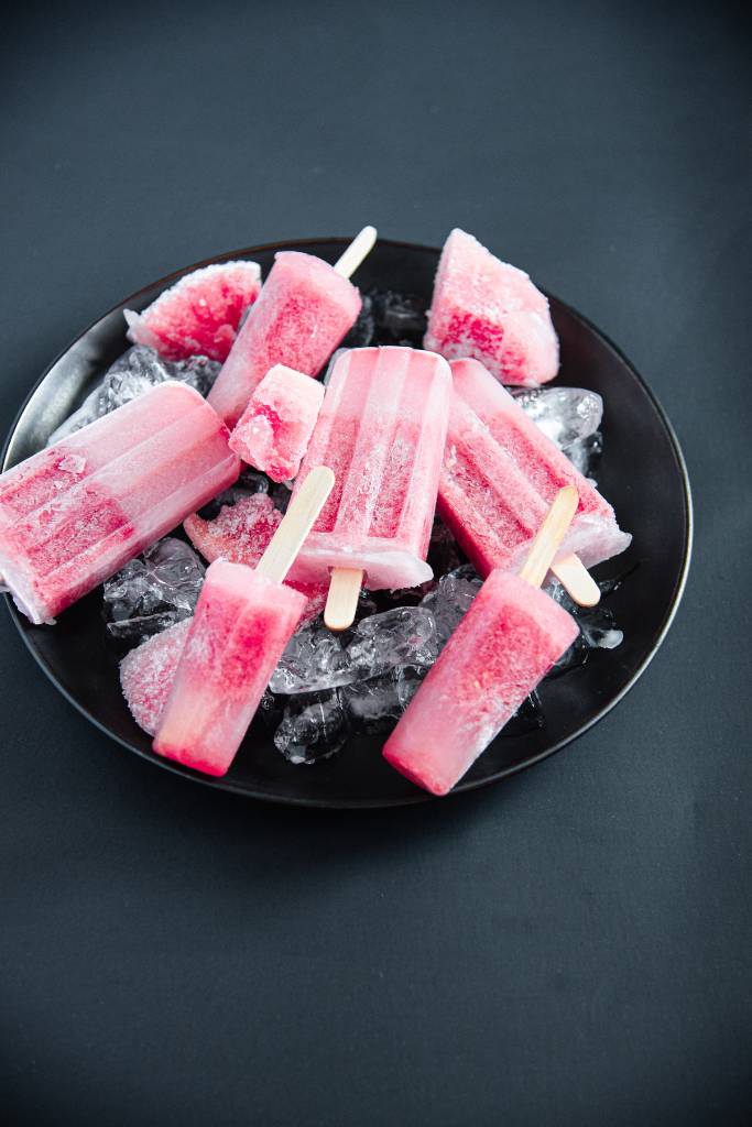 a bunch of popsicels with from frozen watermelon chunks on a black plate full of ice 