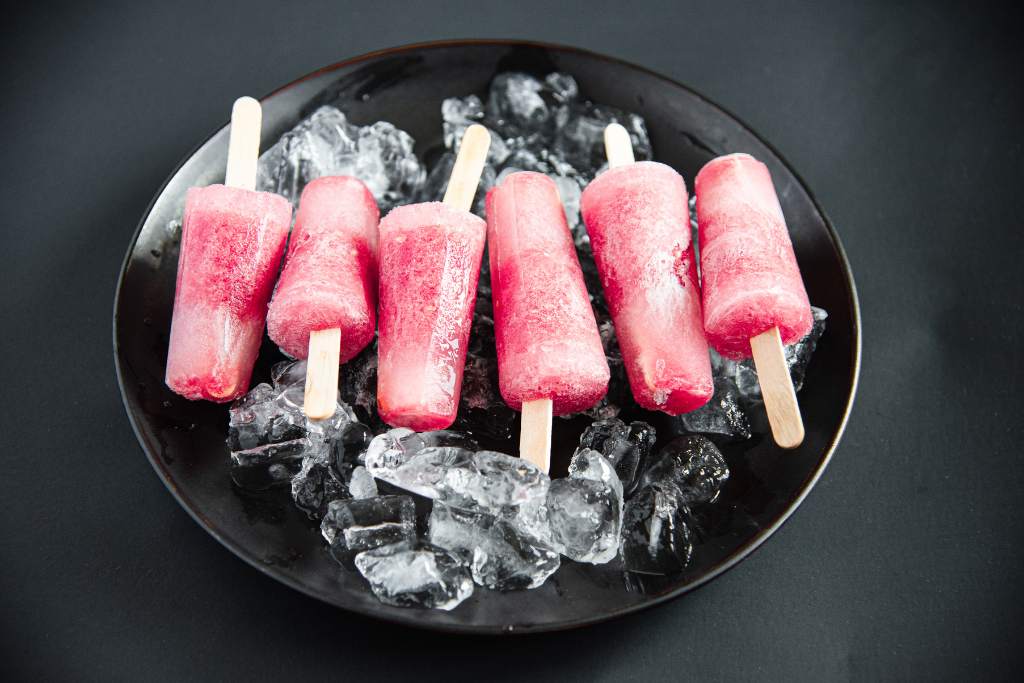 six round popsicles lined up on a black plate of ice 