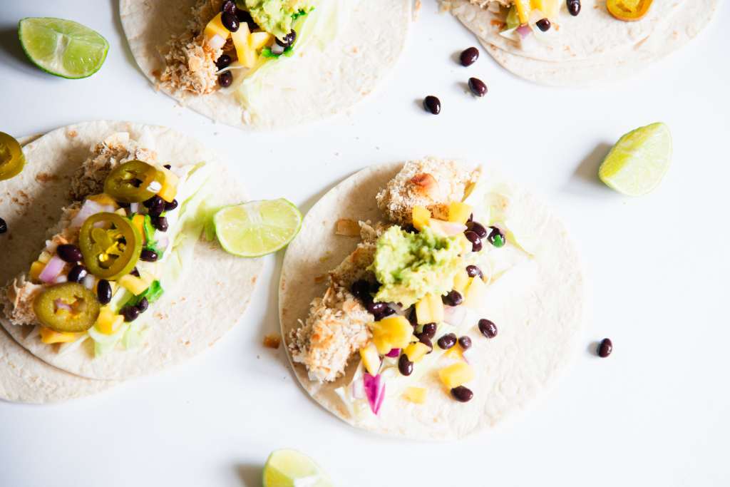 four tacos laying open on a table with some black beans and lime wedges around them