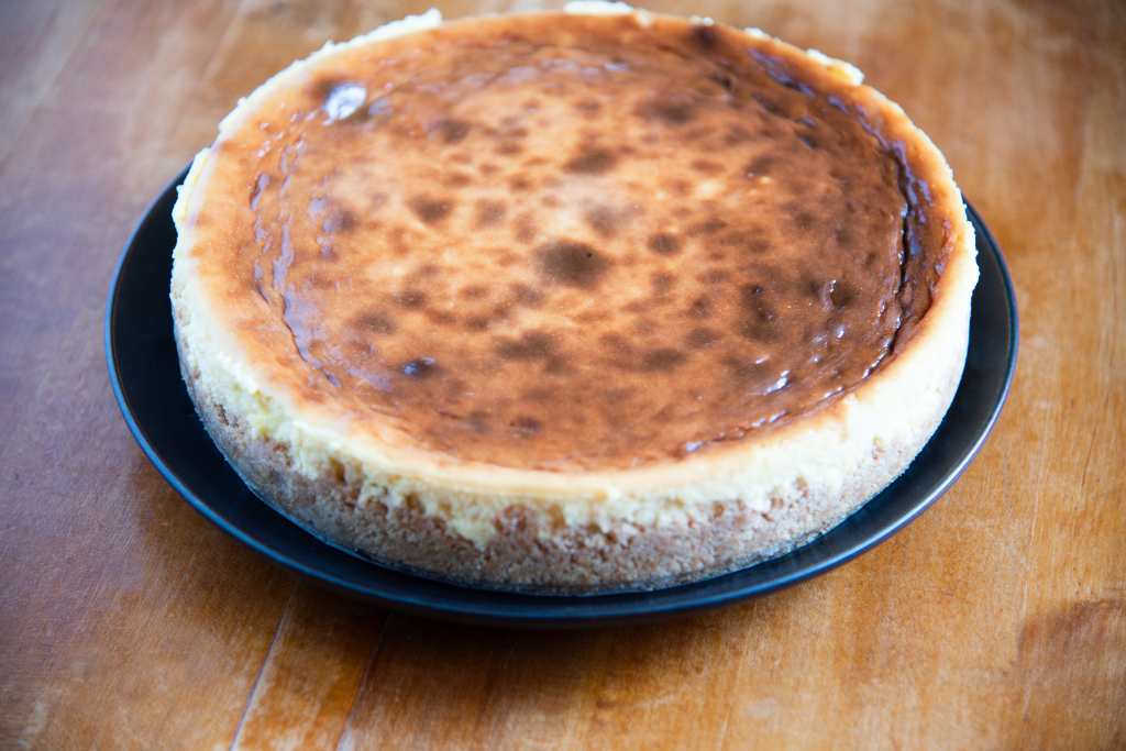 an overhead picture of an uncut cheesecake on a black plate 
