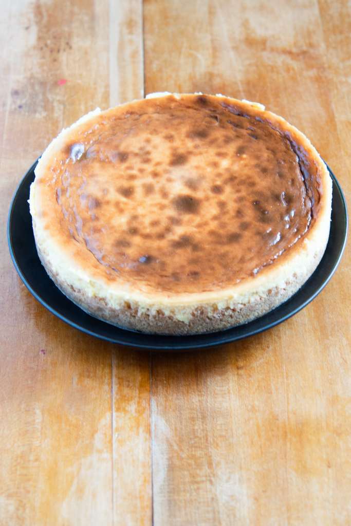 an overhead photo on an uncut cheesecake on a black plate 