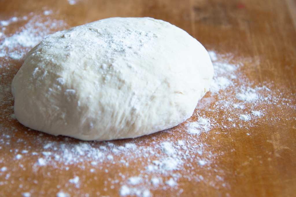 a ball of pizza dough on a wooden table with flour sprinkled on top of it and around it 