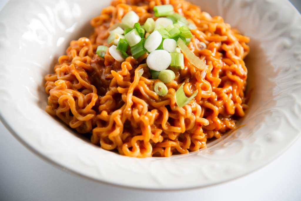 a close up of a while bowl of spicy peanut ramen with sliced green onions on top