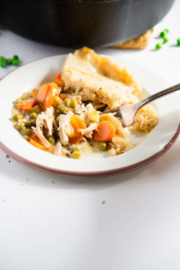 a close up of a fork full of chicken pot pie, resting on a plate of pot pit, you can see part of a pan and a few peas in the background 