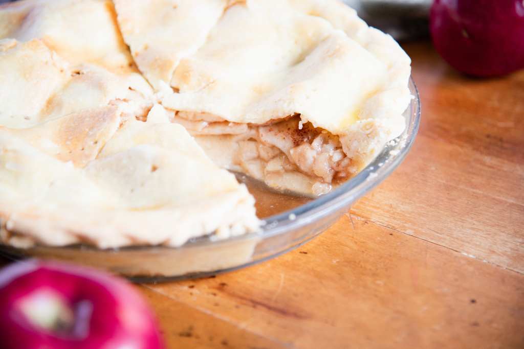 a close up of an apple pie with a piece taken out of it, there are a couple whole apples near the pie in the photo as well 