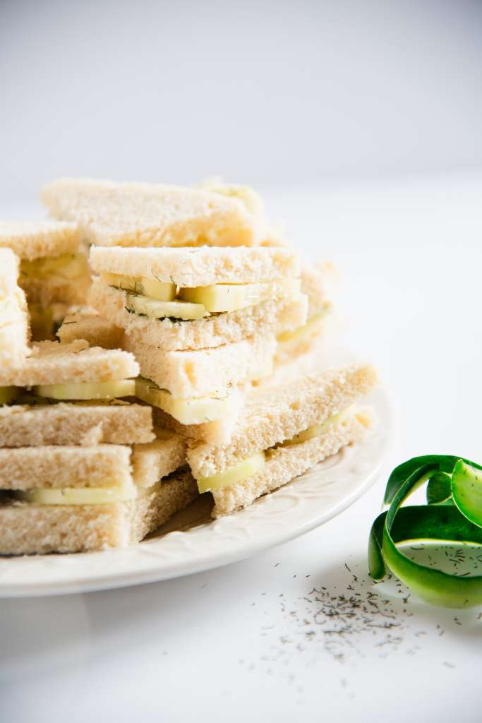 a close up of stacked cucumber sandwiches on a plate with cucumber peels and dill weed next to it 