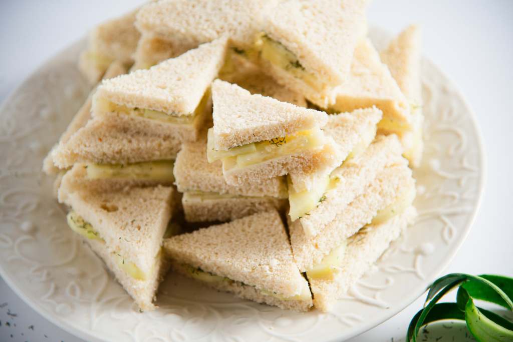 a bunch of cucumber sandwiches stacked on top of each other on a white plate, there are some cucumber peels and dill weed by the plate