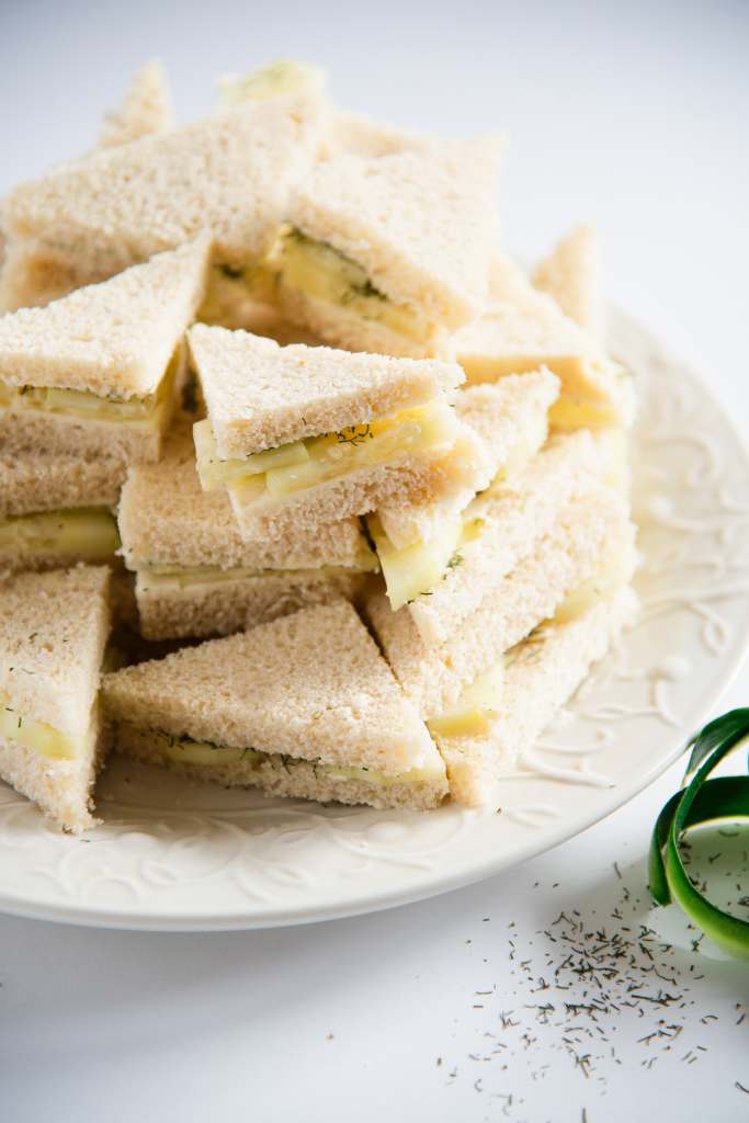 sandwiches on a white plate, with a cucumber peel and some spilled dill weed next to it